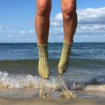 Frau springt in handgestricktn Socken im Meer